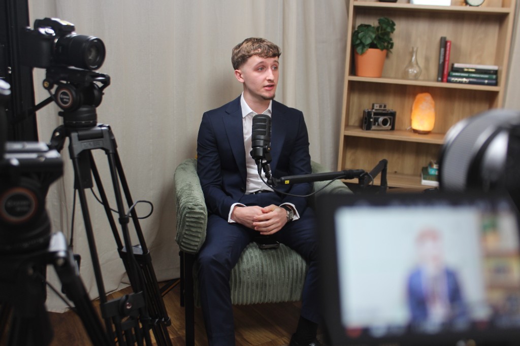 Guest in a suit seated for an Investate podcast interview with cameras set up